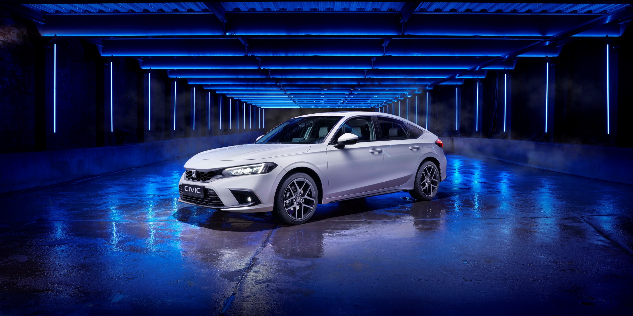 Tříčtvrteční přední pohled na nový model Honda Civic z roku 2022 v bílé barvě, foceno v modře nasvíceném studiu.